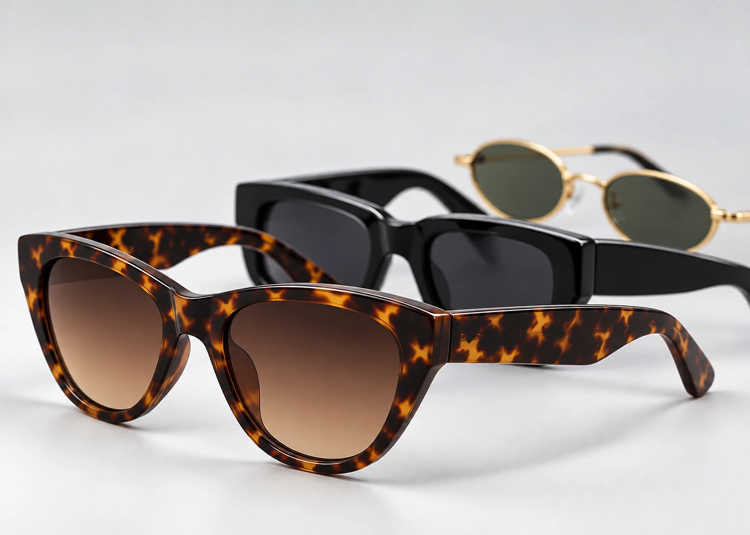 Tortoiseshell cat-eye fashion sunglasses with black rectangular and gold oval frames behind